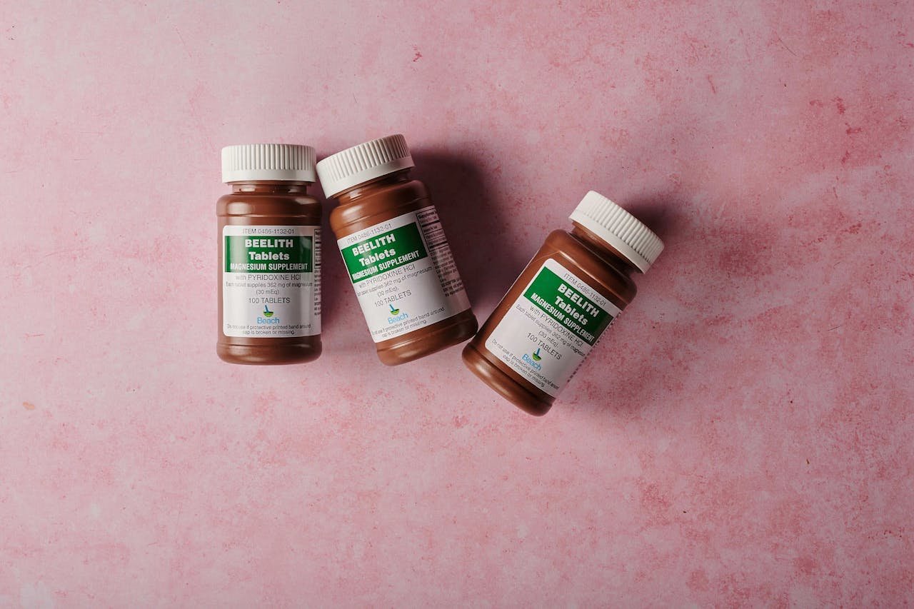 Three brown bottles of magnesium tablets on a soft pink background, ideal for health-themed content.