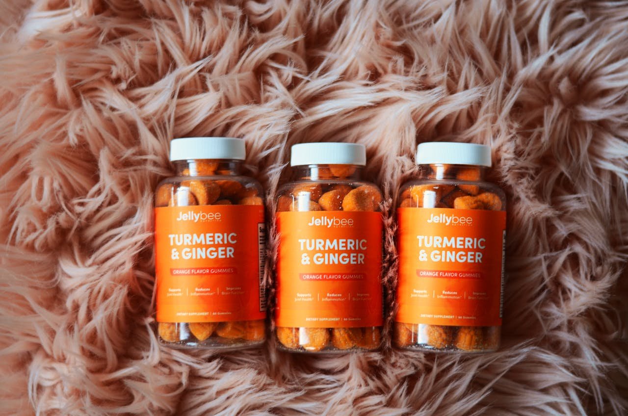 Bottles of orange turmeric and ginger gummies on a plush carpet, promoting health and wellness.